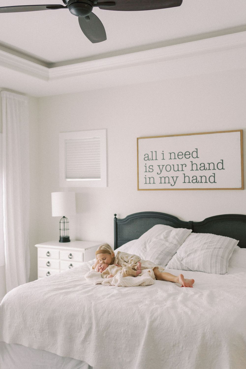 Serene bedroom interior with white bedding and wall art reading 'all i need is your hand in my hand'.