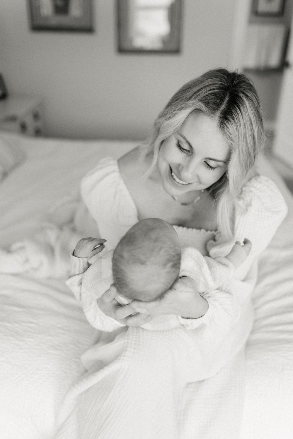 Intimate black and white portrait of parent and baby sharing a tender moment on white bedding.