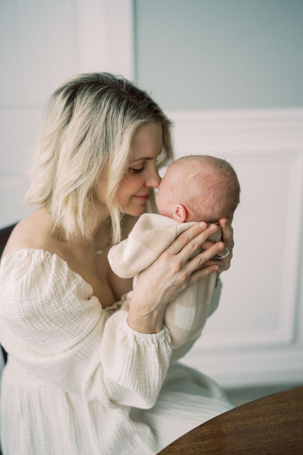 Intimate portrait showing tender moment between parent and baby against white wall.