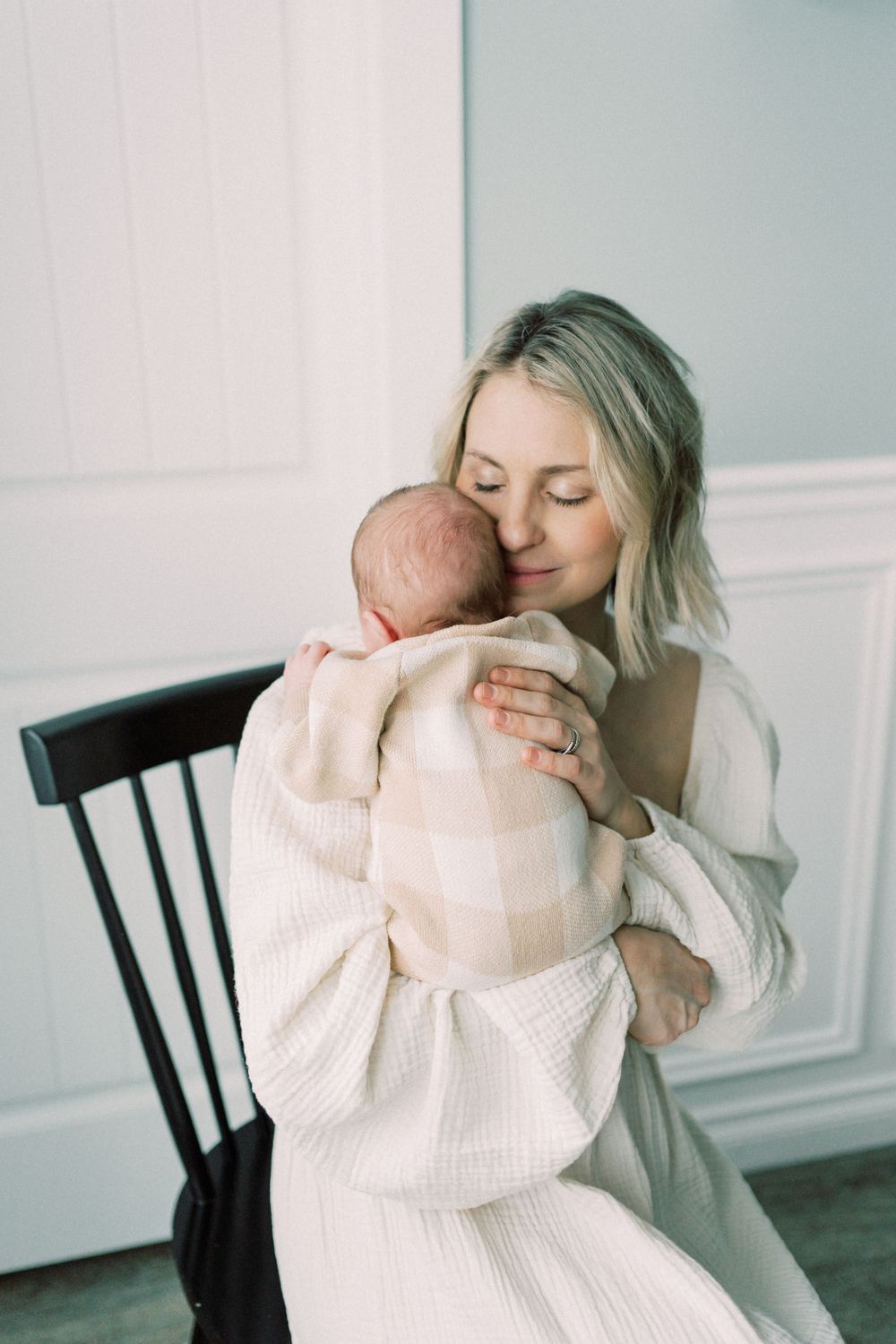 Parent and baby share tender moment while sitting in black chair wearing matching cream knit sweaters.