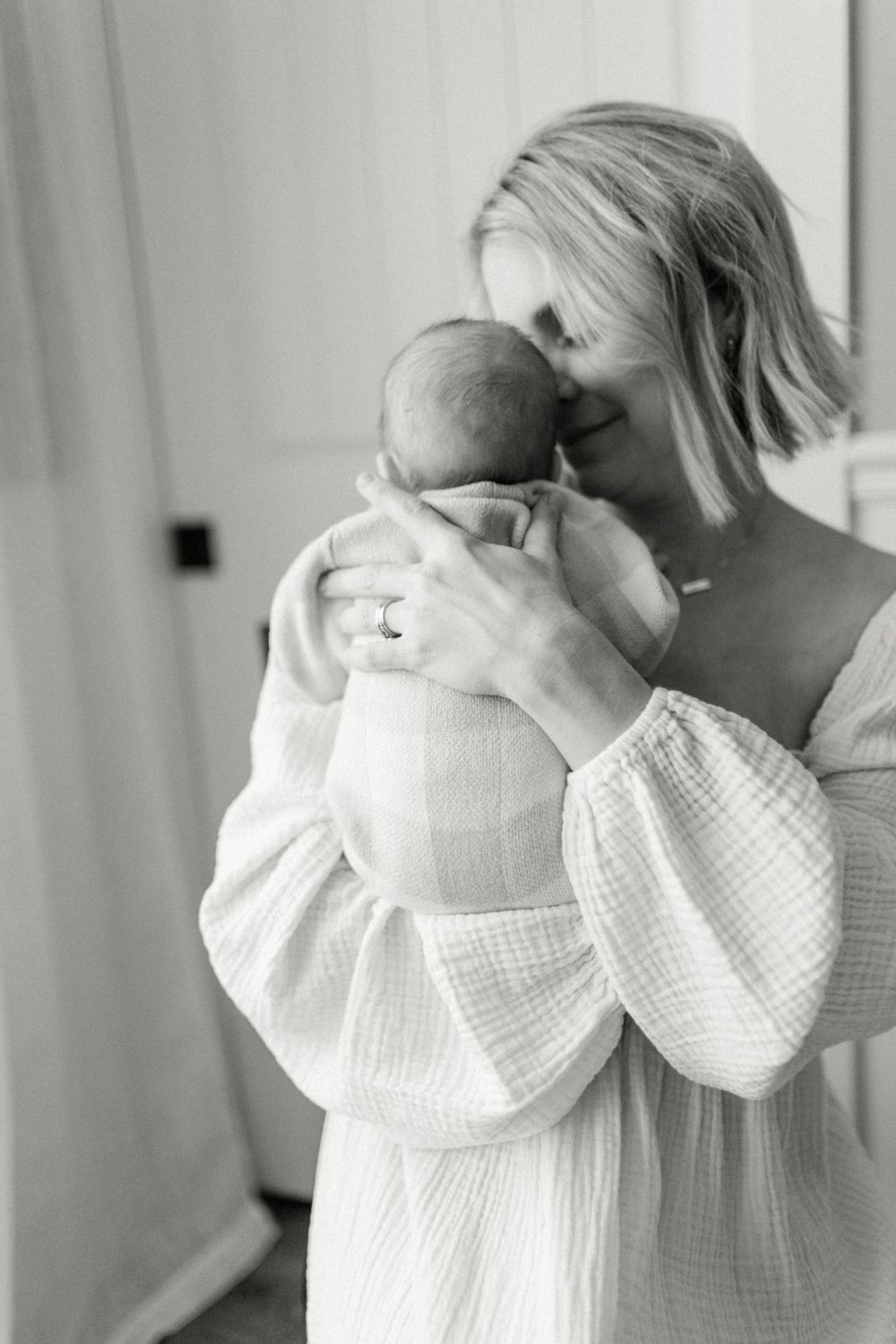 Black and white photo capturing intimate moment between parent and infant in white clothing.
