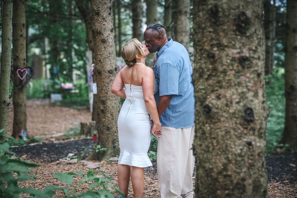 A tender moment shared between a couple standing by a large tree trunk in a wooded outdoor setting.