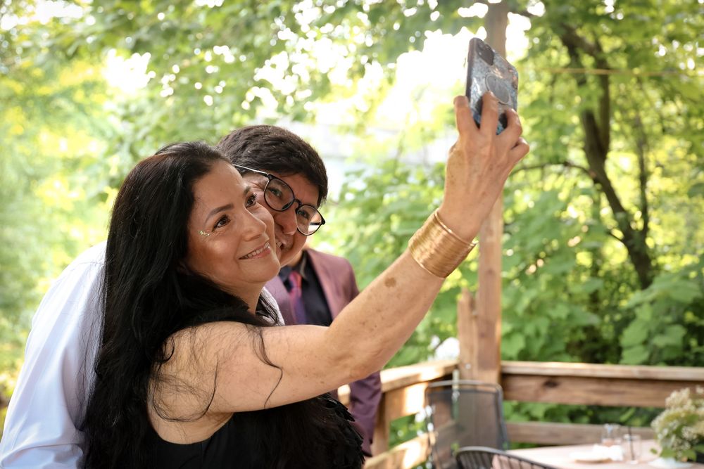 A couple taking a selfie together outdoors in a wooded setting during a summer day.