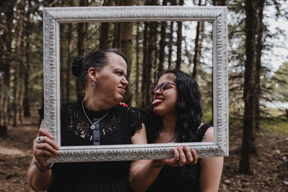 A couple shares a joyful moment while holding a vintage white frame in a forest setting.