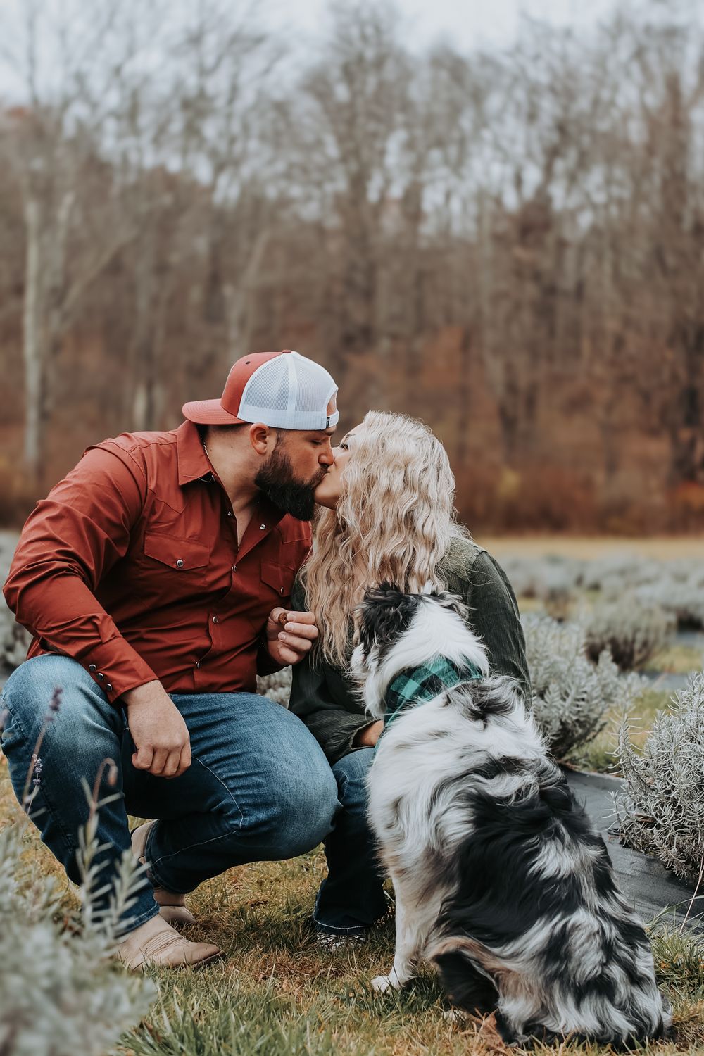 A cozy couple and their Australian Shepherd dog share a sweet moment together in a rustic outdoor setting.