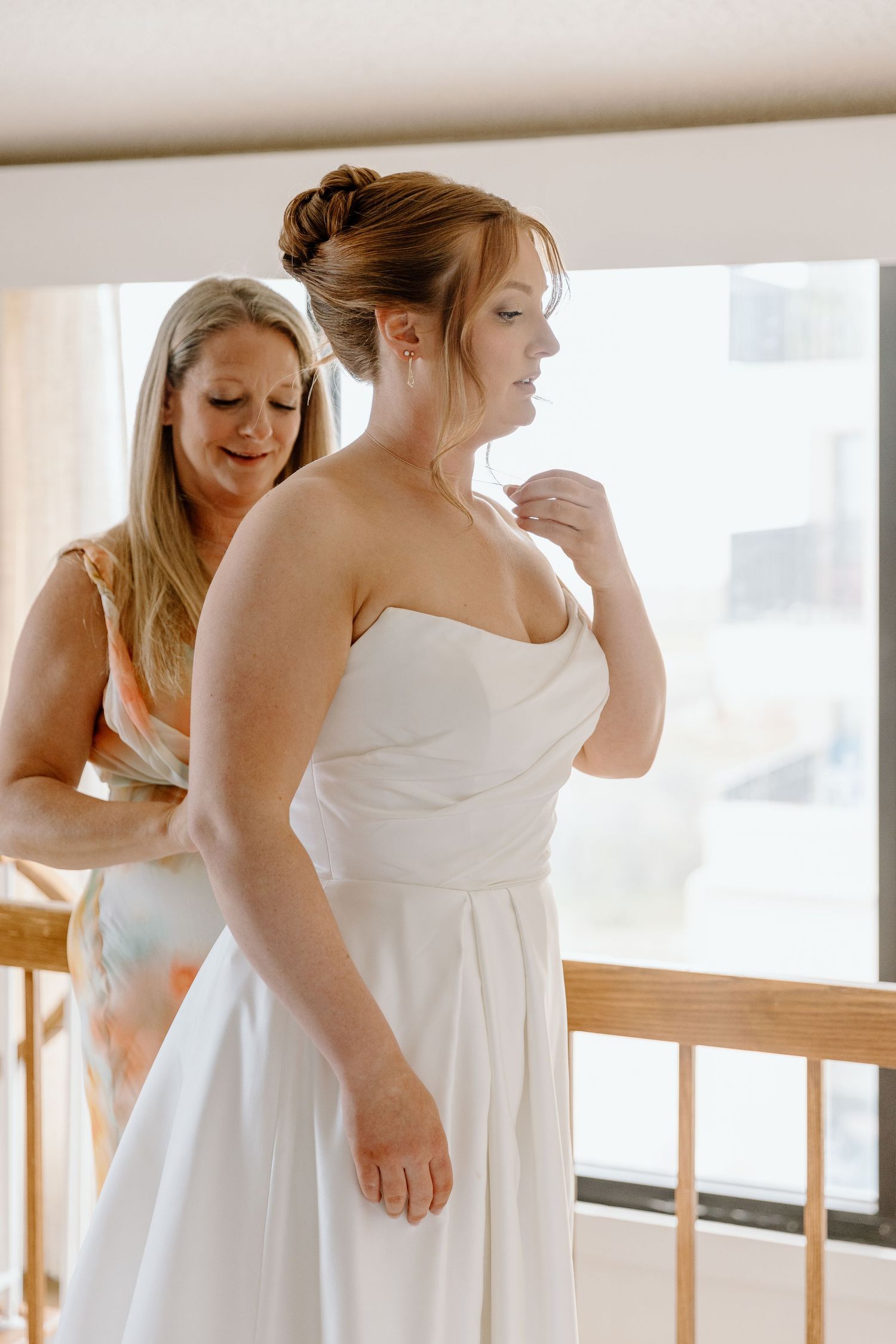 A bride in a white wedding dress stands while being fitted and adjusted during a pre-wedding preparation moment.