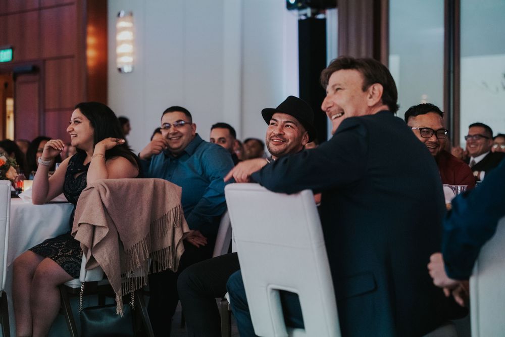 An attentive audience seated in white chairs reacts with laughter during an indoor event or presentation.