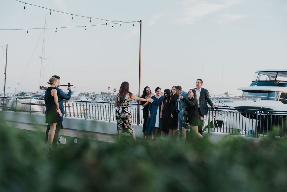 Wedding guests gather on an outdoor rooftop deck with string lights and city views during a celebration.