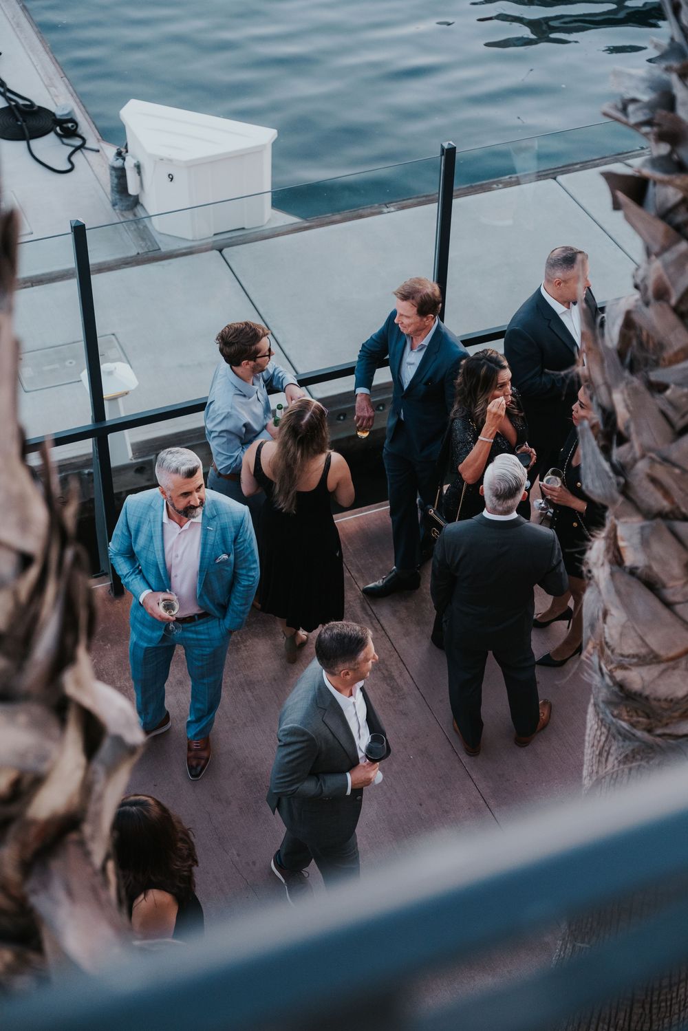 High-angle view of people gathered at a waterfront deck for an elegant outdoor social event near the marina.