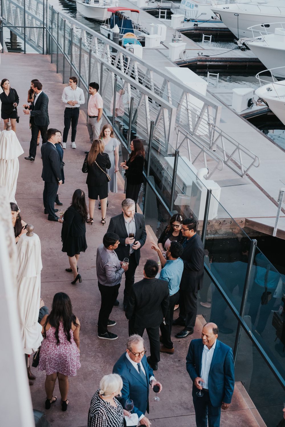 People gathered at an upscale marina dock area for a networking event near luxury yachts and boats.