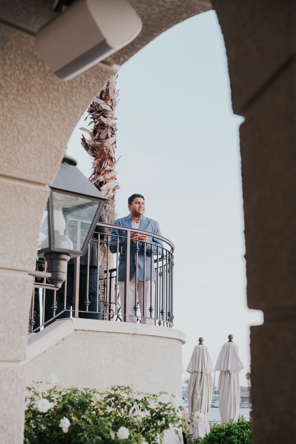 A person stands on a white Mediterranean-style balcony with arched architectural features and decorative railings.