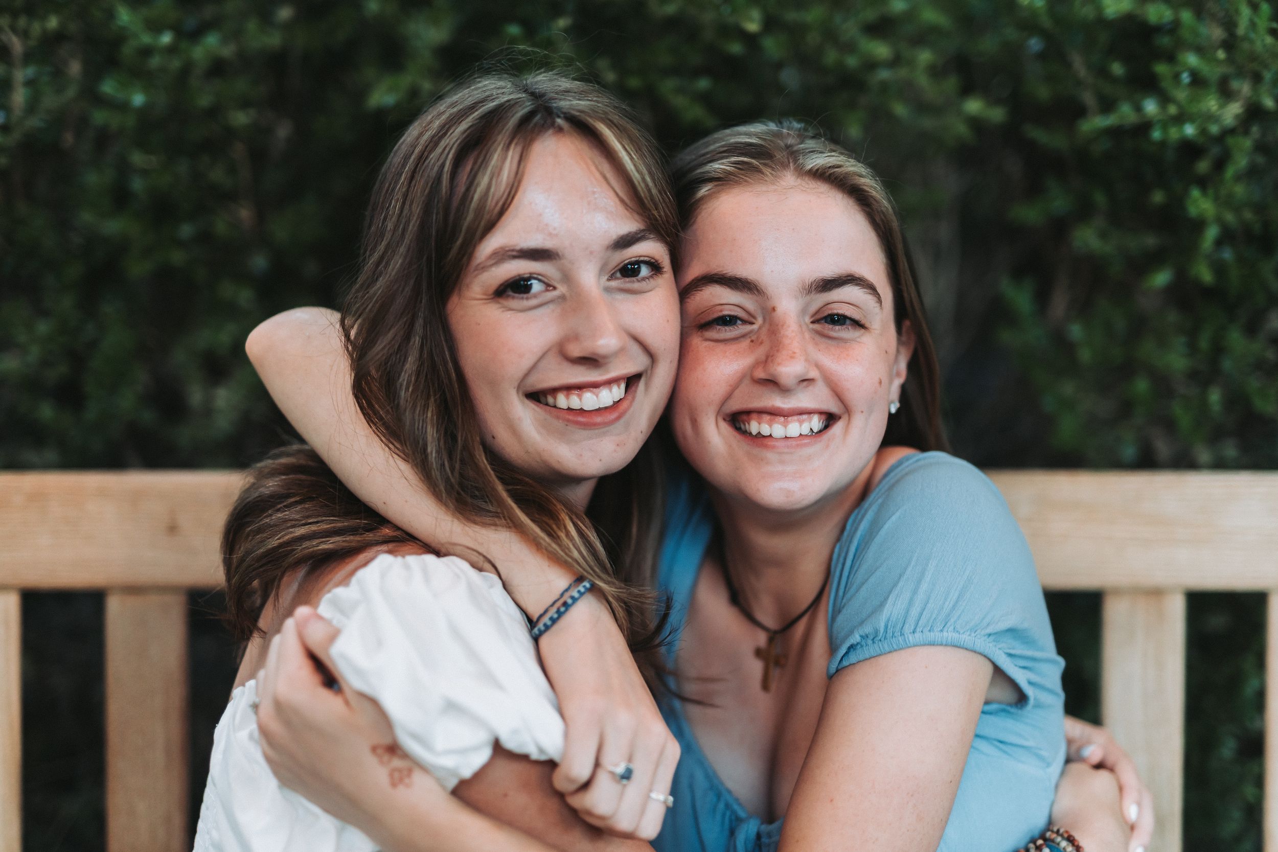 Two friends embrace and laugh together while sitting outdoors.