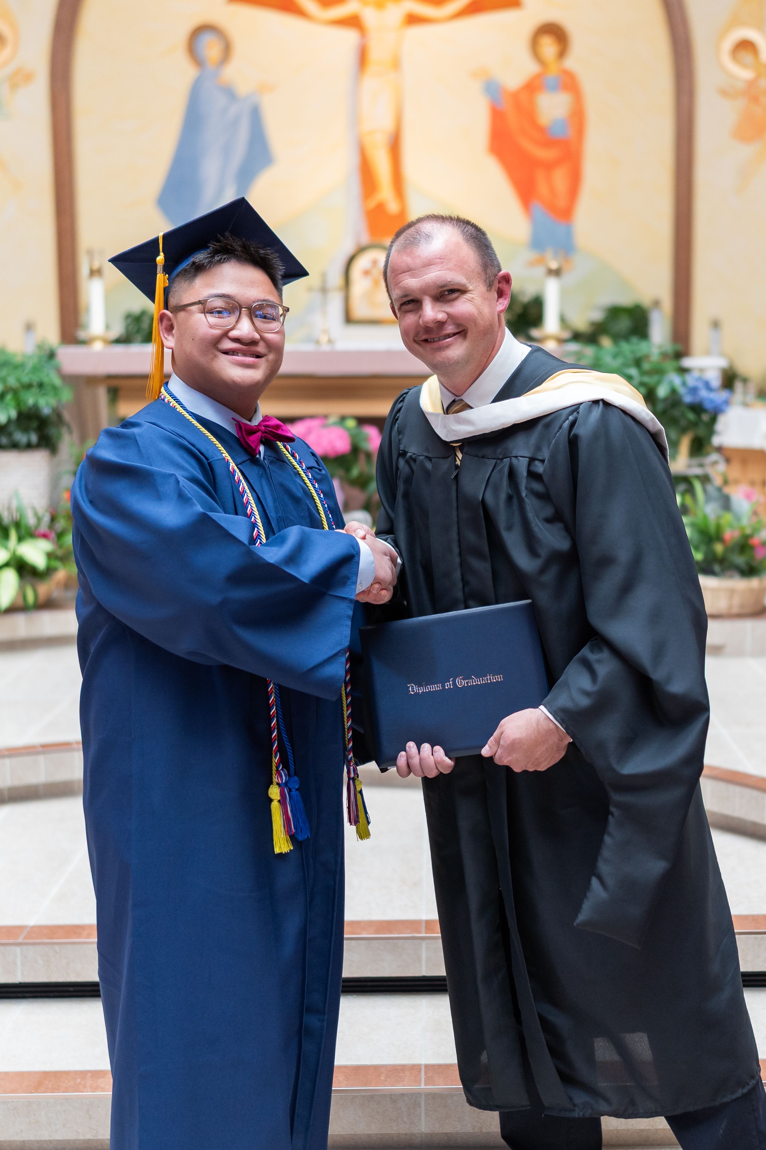 Graduation ceremony with graduate and faculty member shaking hands in church setting.