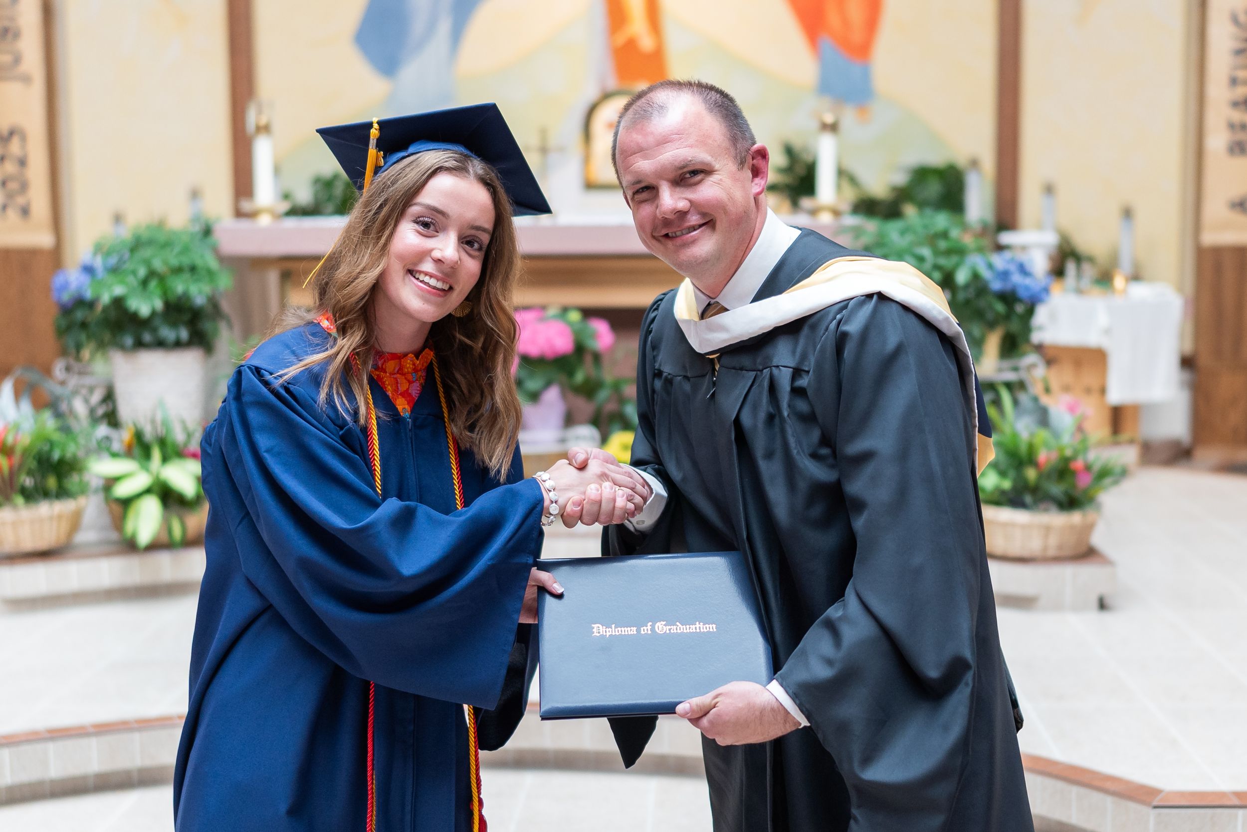 Graduate receives diploma and handshake in church sanctuary.