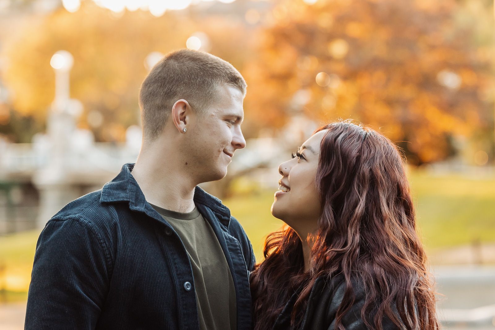 A romantic couple sharing a tender moment in an autumn park with golden foliage in the background.