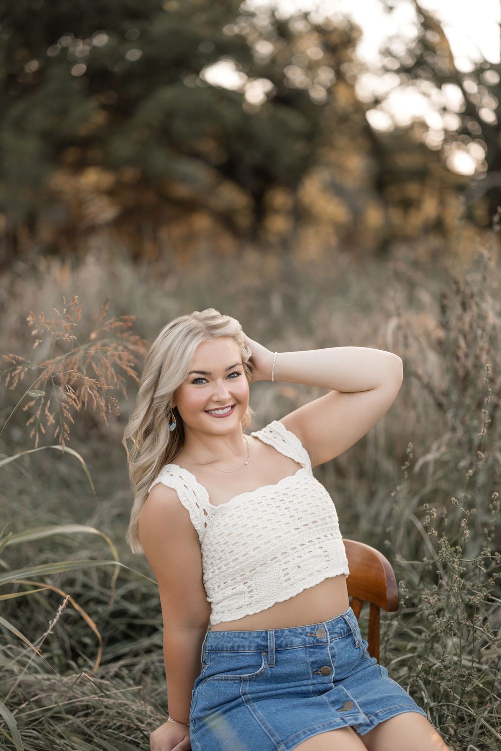 A summer portrait in a rustic field features a white crop top and denim skirt outfit.