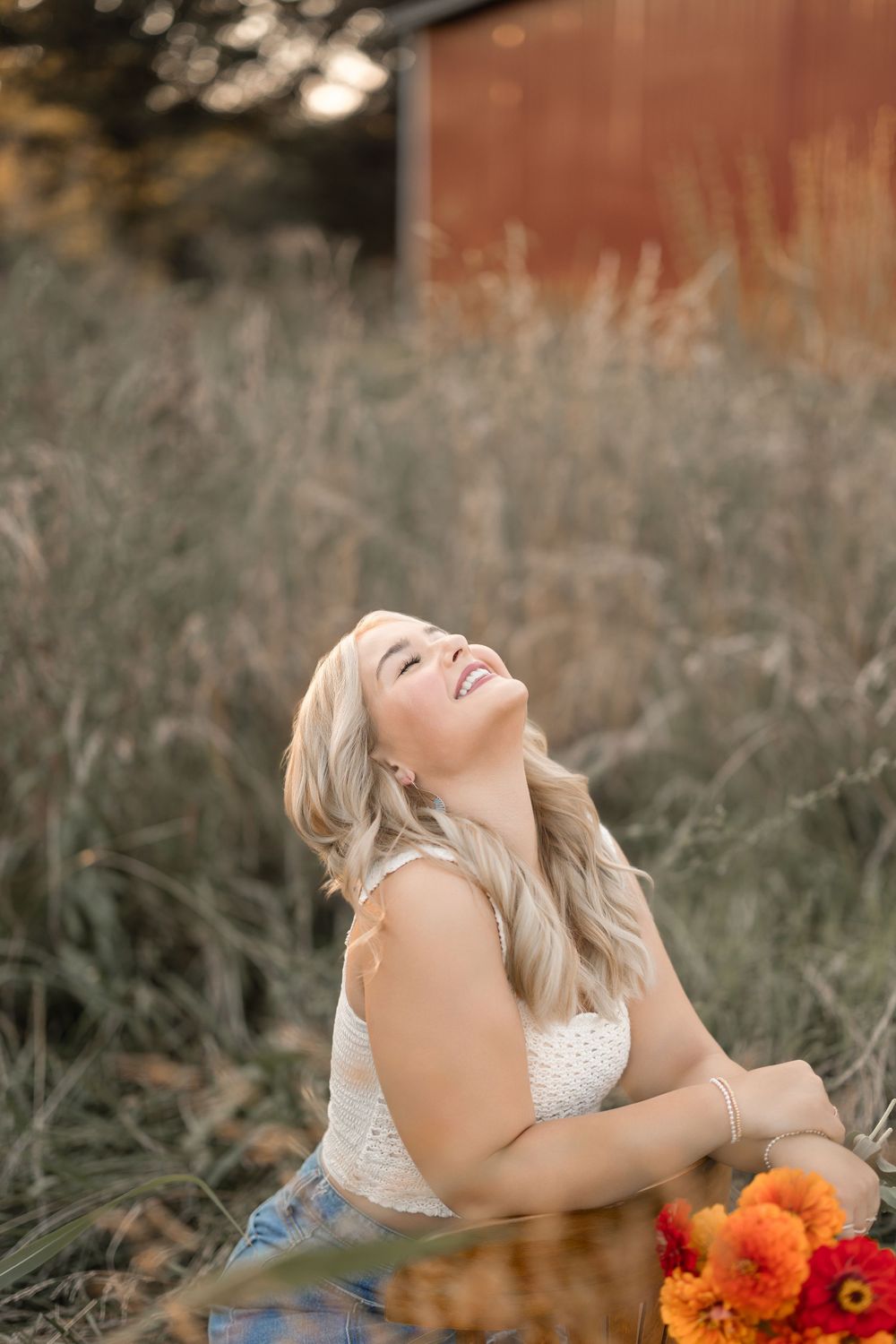 Joyful summer portrait with rustic barn backdrop and bright orange flowers in golden sunlight.