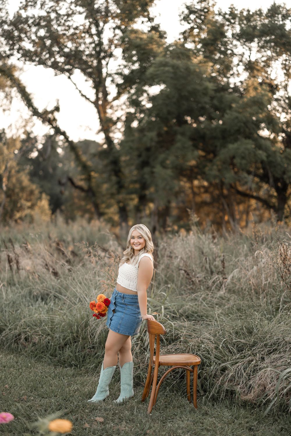 Rural sunset portrait with light blue boots, denim skirt and wooden chair among tall grasses.