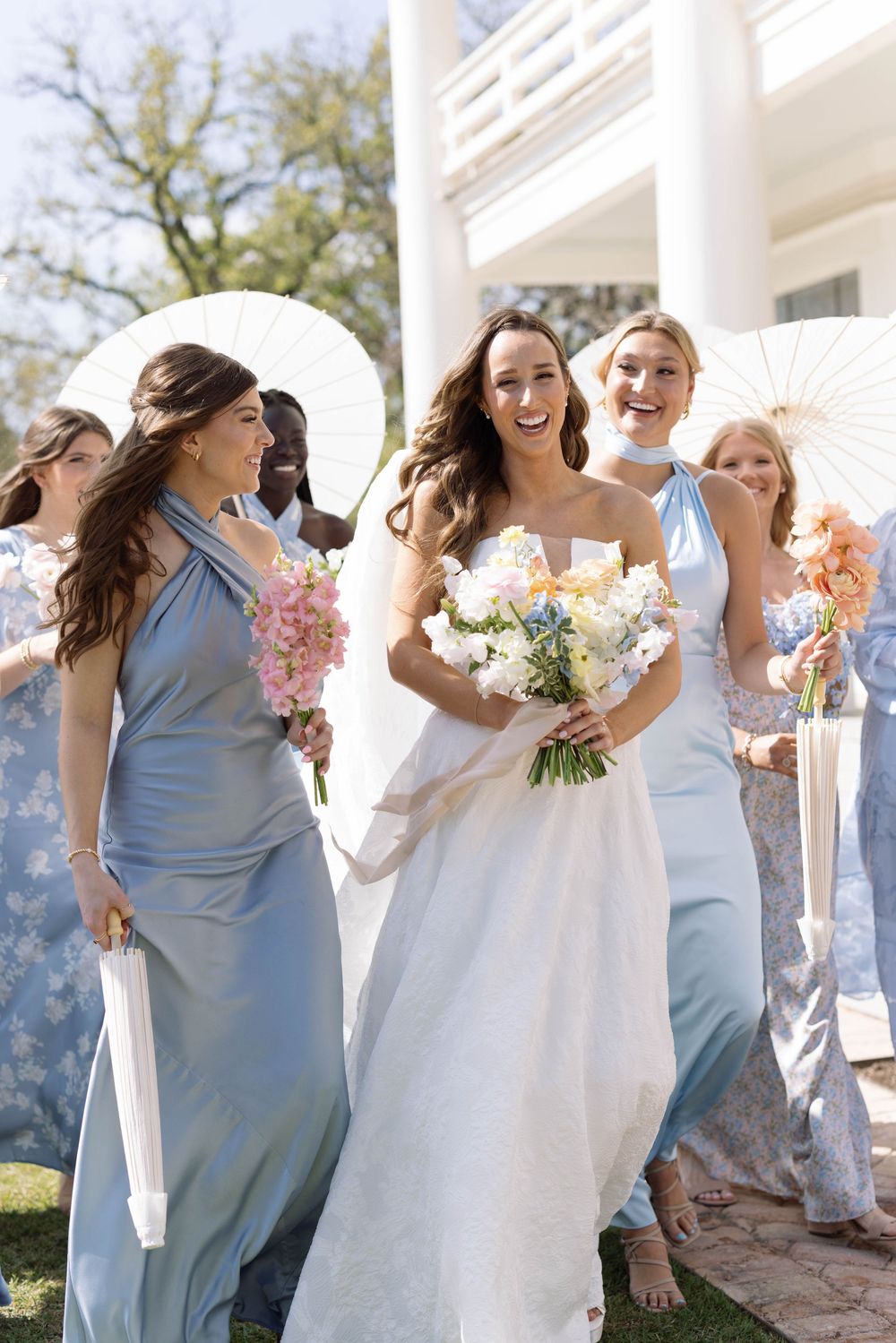 Bridesmaids in light blue dresses laugh and dance together in a candid photo sequence outside a white columned building.