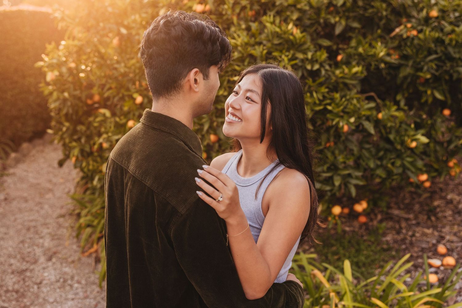 A couple embraces outdoors during golden hour sunlight in a garden setting near flowering orange trees.