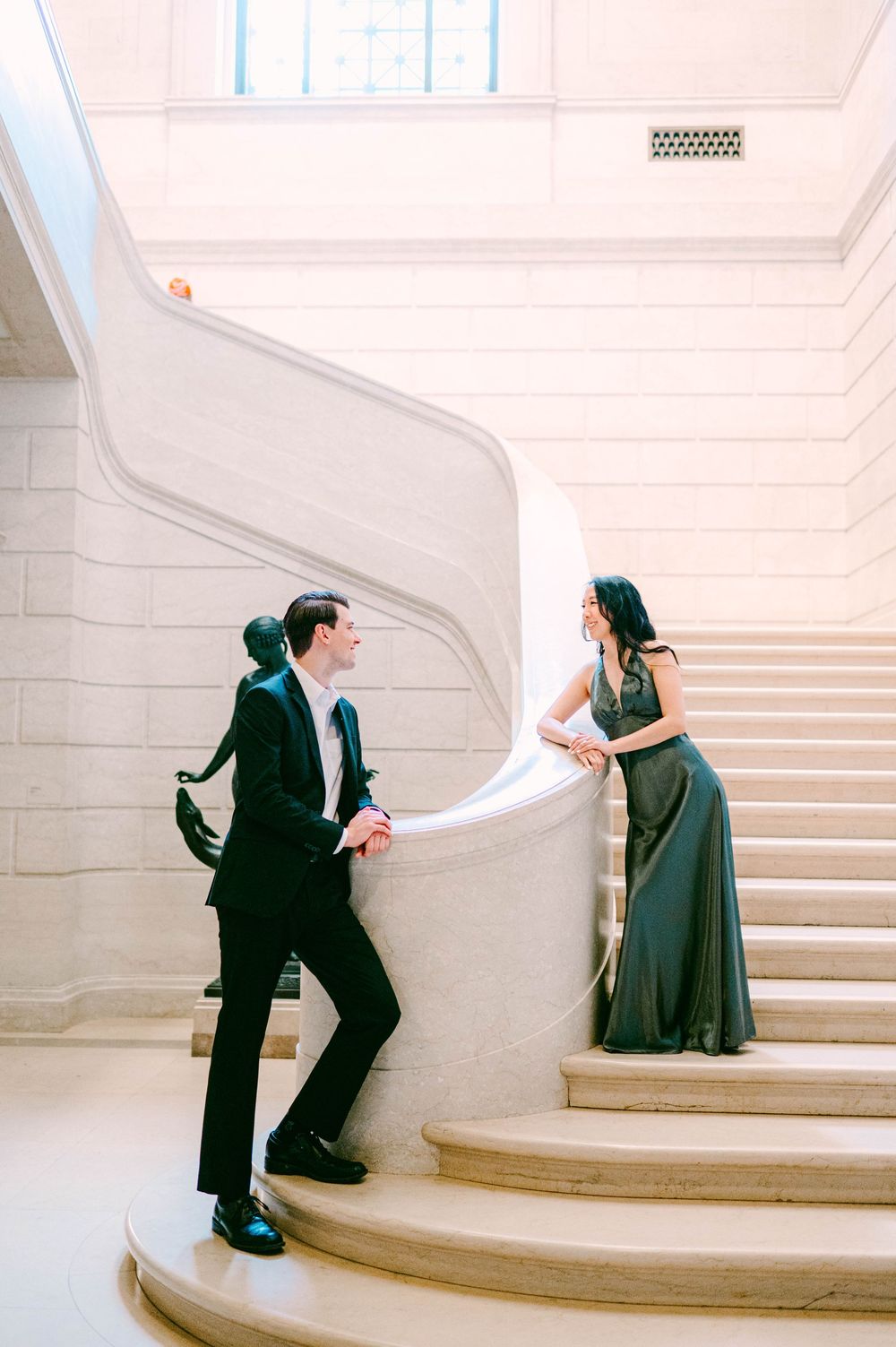 Couple executing graceful dance poses on curved marble staircase in bright interior.