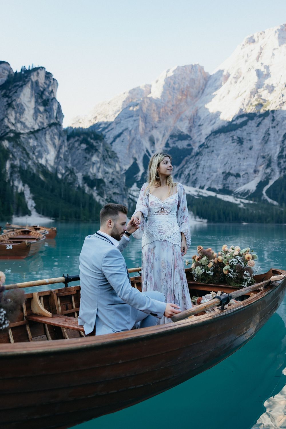 A romantic proposal moment on a wooden boat at turquoise Lago di Braies with dramatic Dolomite mountains in the background.