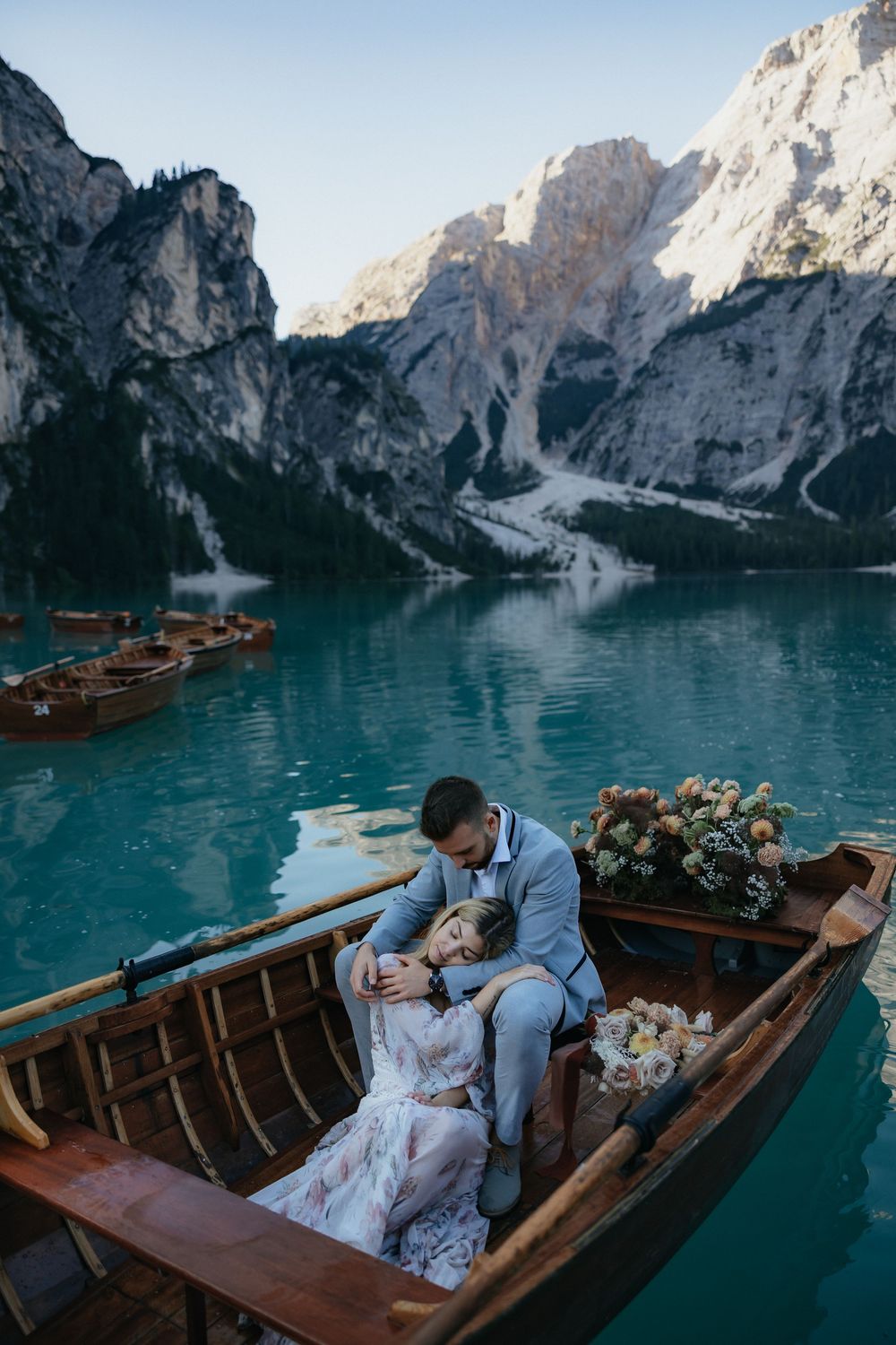 Couple shares romantic moment in wooden boat on turquoise alpine lake surrounded by dramatic mountain peaks.