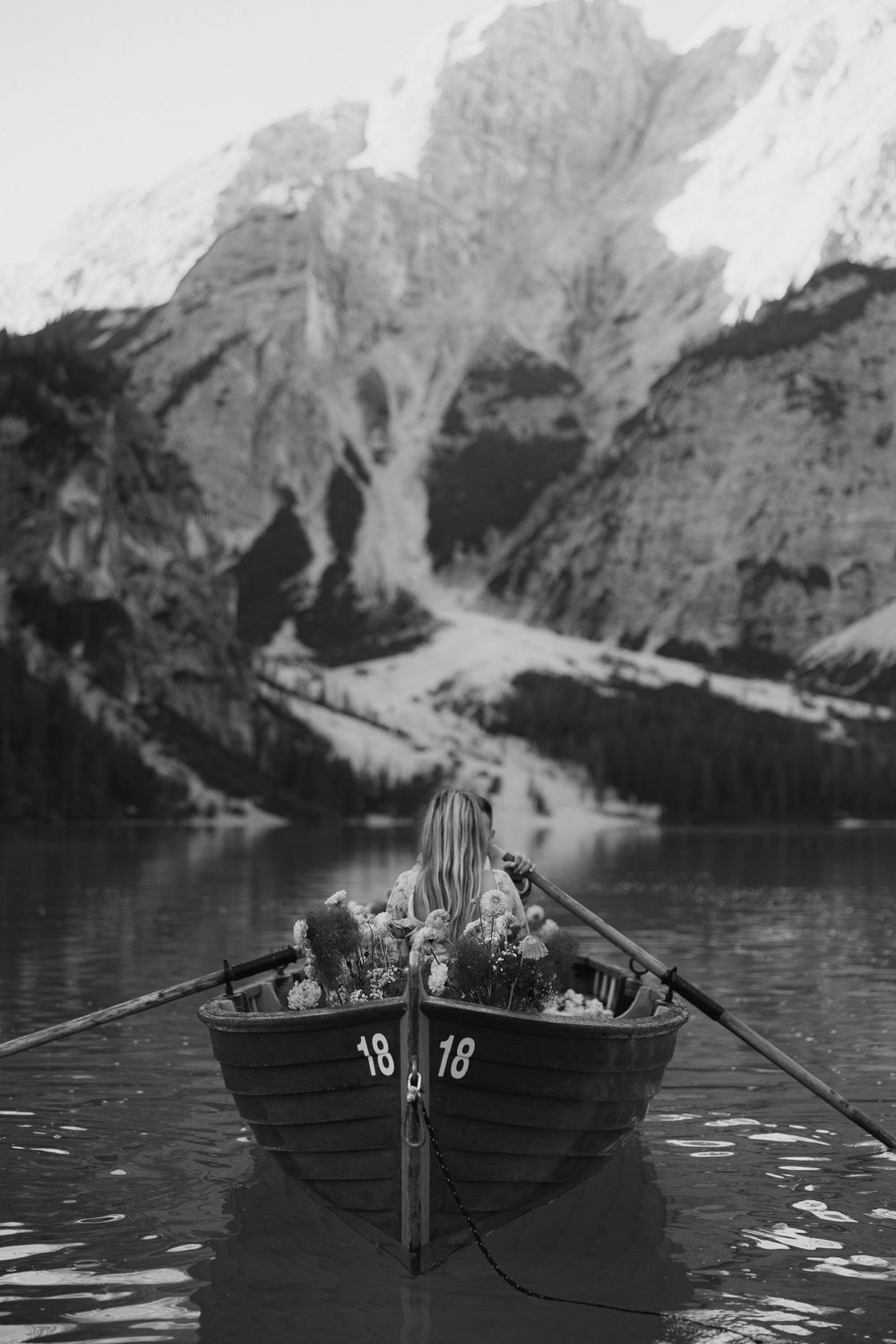 A wooden boat on a mountain lake surrounded by towering peaks in black and white photography.