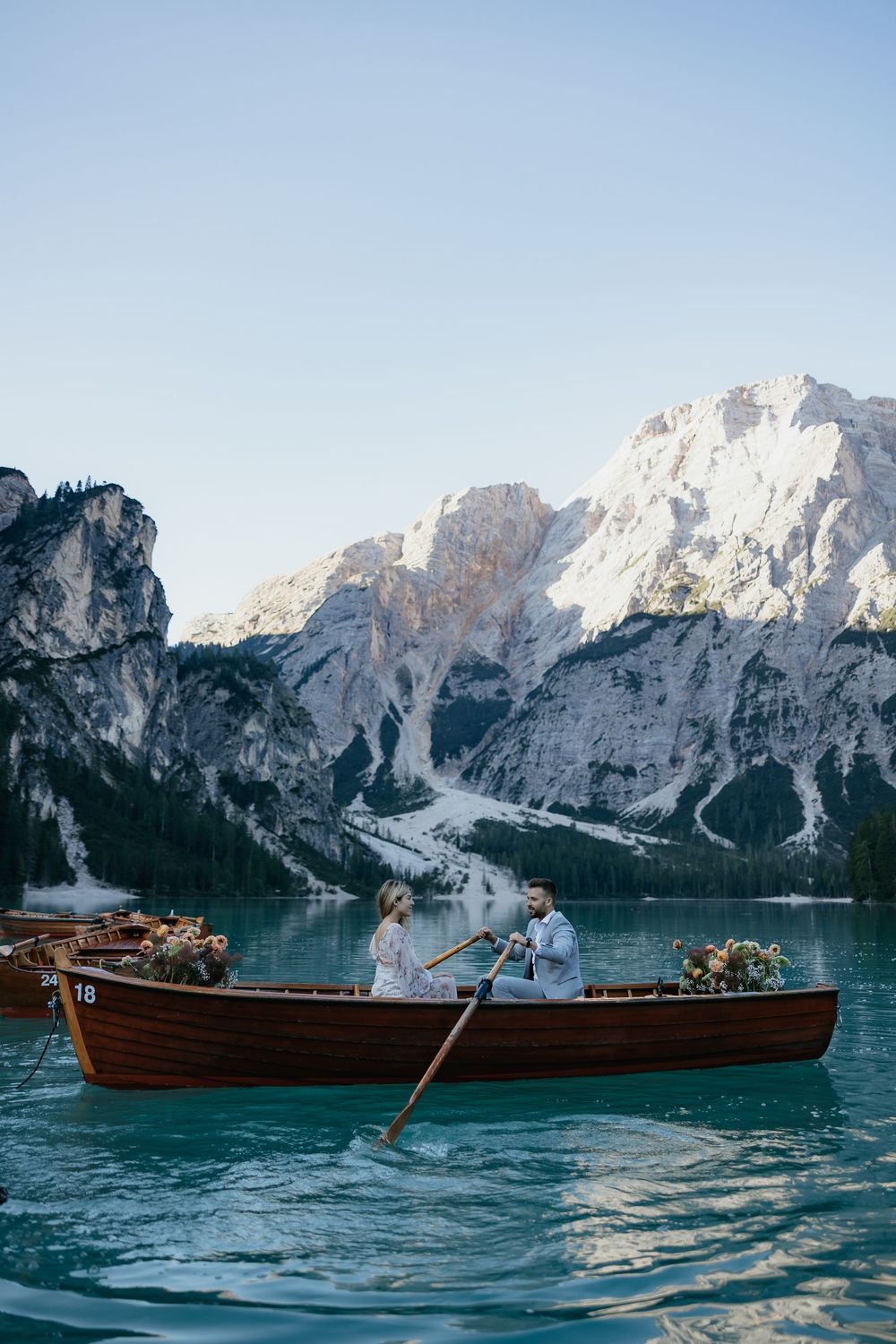 A wooden row boat floats on turquoise waters of Lake Braies in the Dolomites with dramatic mountain peaks in background.