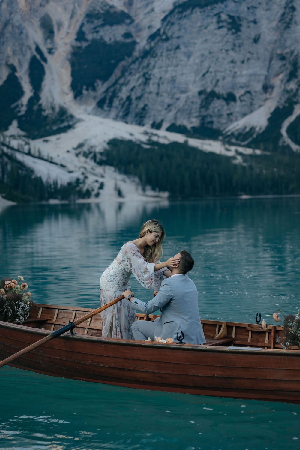 A romantic moment captured on a wooden boat floating on turquoise alpine lake with mountain backdrop.