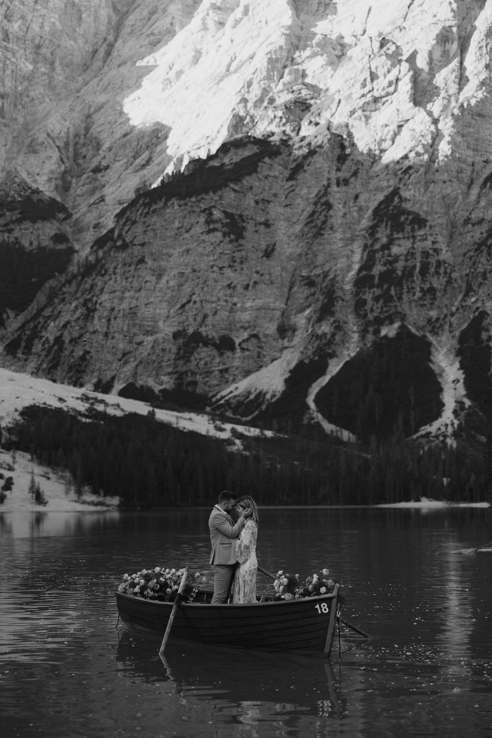 A couple sharing an intimate moment in a wooden boat on a scenic mountain lake in black and white.