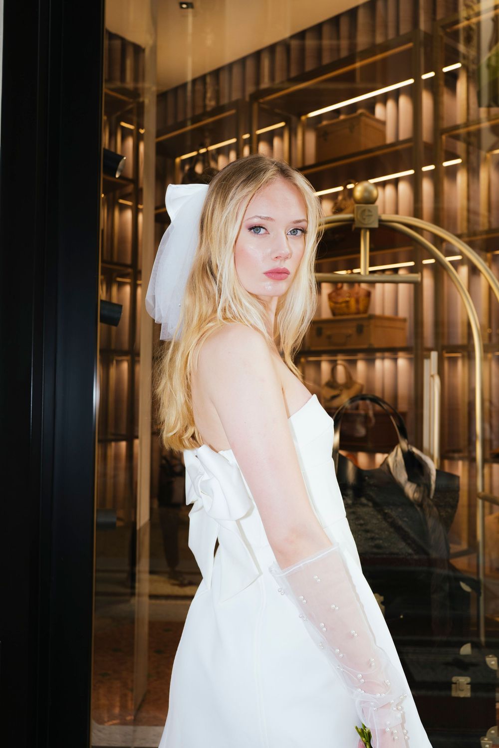 A woman in a flowing white dress poses gracefully against an industrial setting with metal bars and columns.