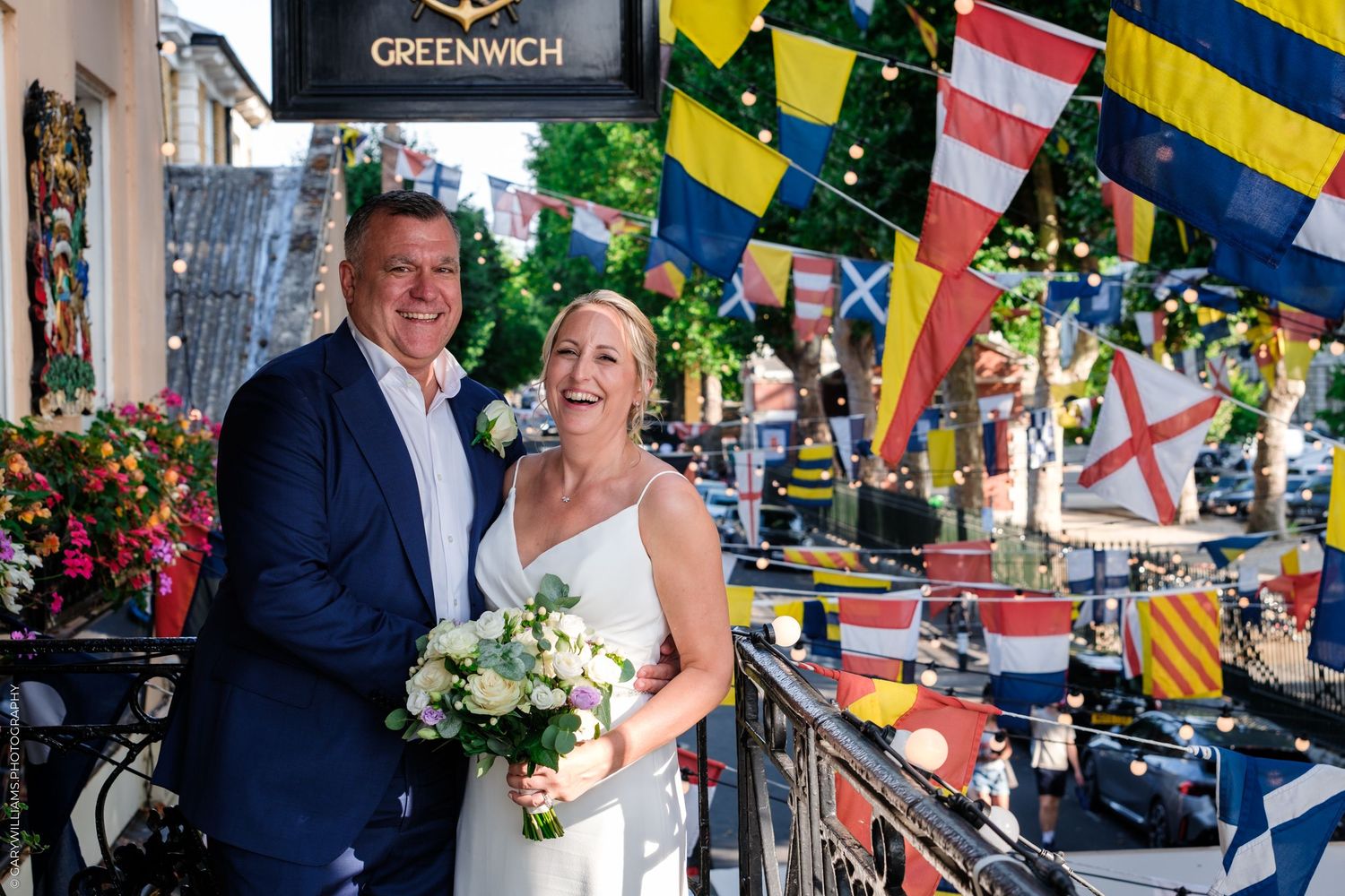 Wedding party celebrates under colorful nautical flags at outdoor seaside venue in Greenwich.