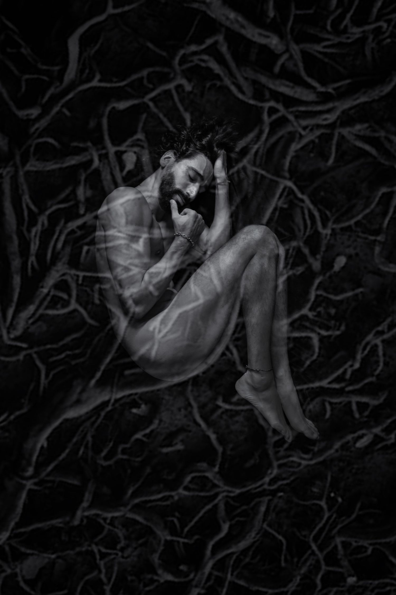 A haunting black and white artistic photograph showing a figure curled up among dark twisted tree branches.