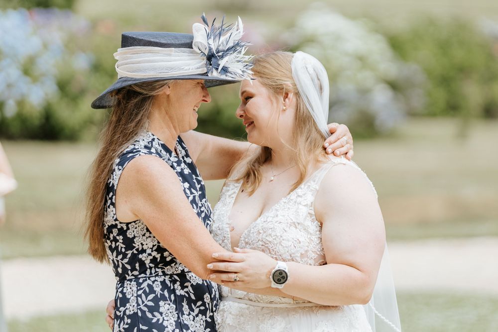 Two wedding attendees share an intimate moment while dressed elegantly outdoors on a sunny day.