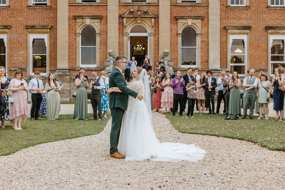 Wedding guests line up along a curved path for a traditional toss celebration at a historic brick manor house.