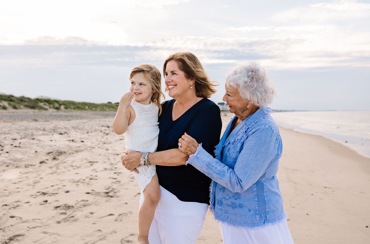 Three generations walking together on a sandy beach at sunset with the ocean in the background.