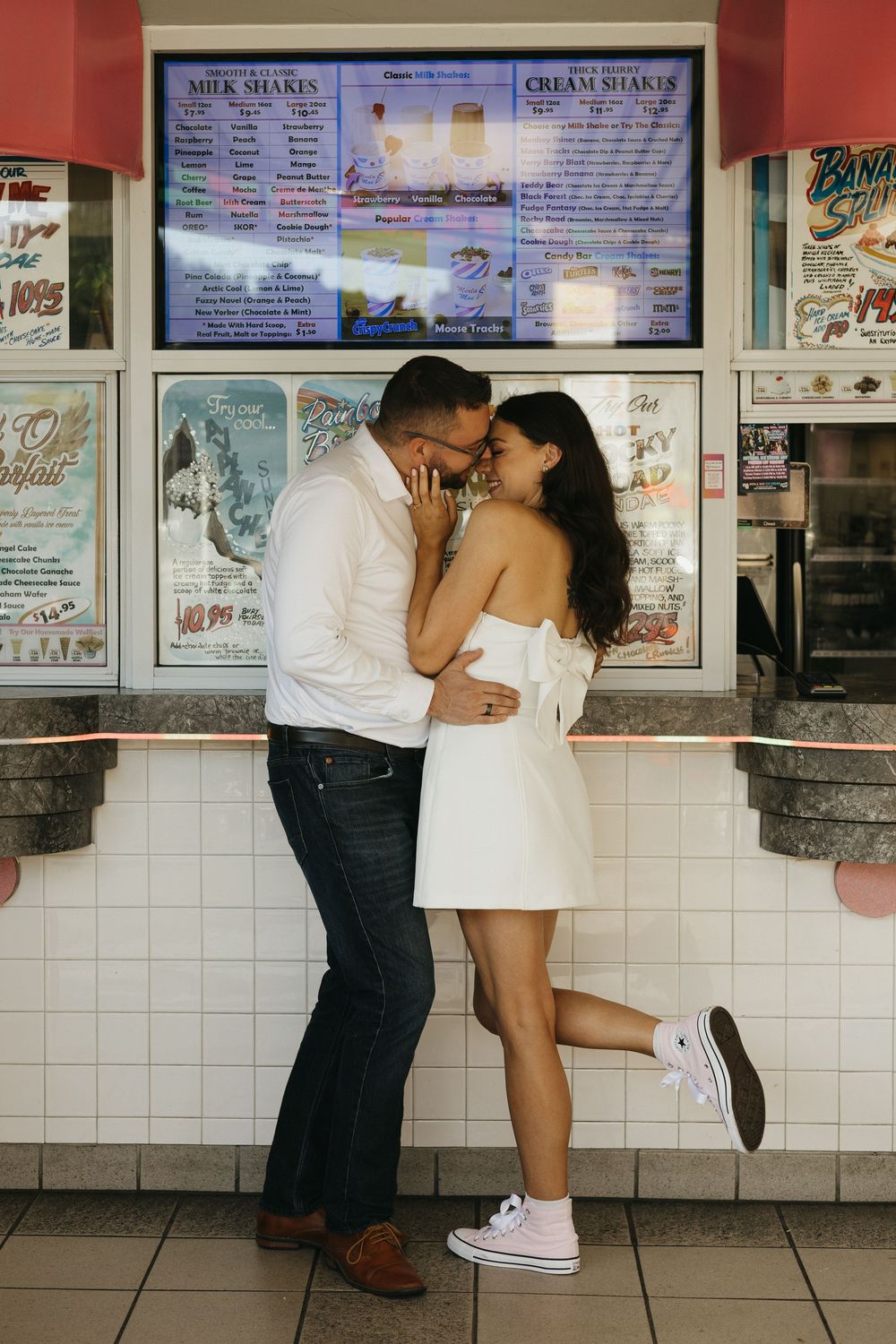 Romantic couple sharing an intimate moment at an ice cream shop counter with menu boards displayed above.