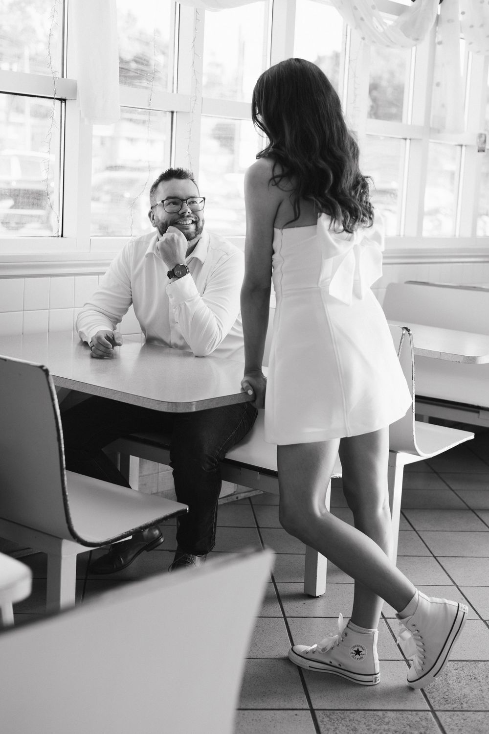 Black and white photo of casual interaction in Merla Mae showing two people at table, one wearing white Converse sneakers. London Ontario