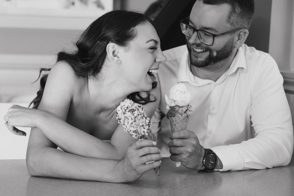 Black and white photo of a couple laughing together while sharing ice cream cones at a table. London Ontario Engagement Photos
