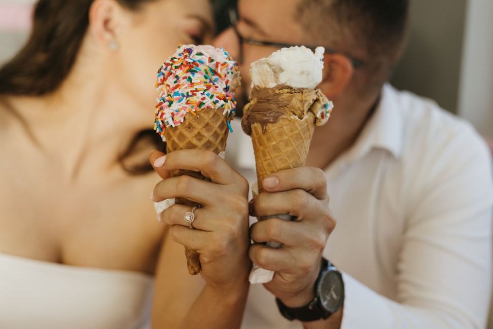 Two hands hold ice cream cones topped with colorful sprinkles and whipped cream in a romantic close-up shot. London Ontario Engagement Photo