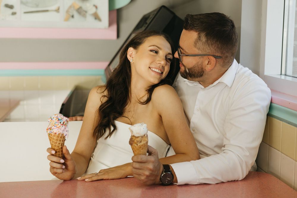 A couple shares an intimate moment while enjoying ice cream cones together in a pastel-colored cafe setting.