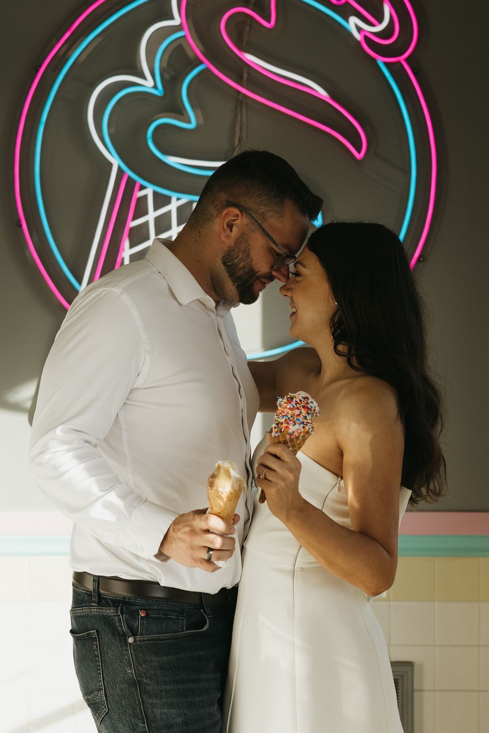 Romantic couple sharing ice cream cones under a neon flamingo sign at an ice cream shop. London Ontario Wedding Photography