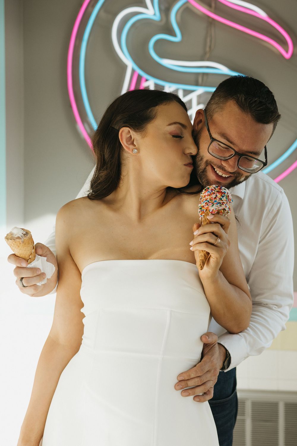 A couple sharing playful moments while eating donuts against a neon-lit background.