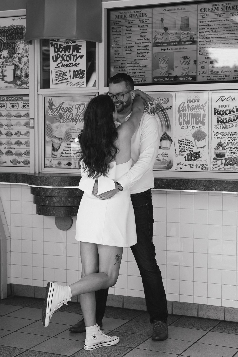 A series of black and white photos showing two people embracing in front of a restaurant menu board.
