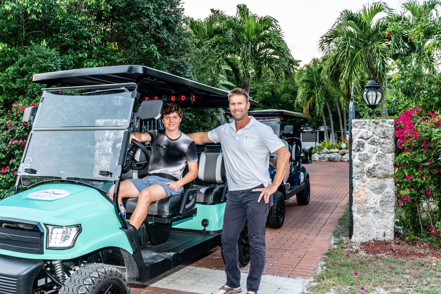 People standing by green golf carts on a palm tree-lined pathway at a resort.