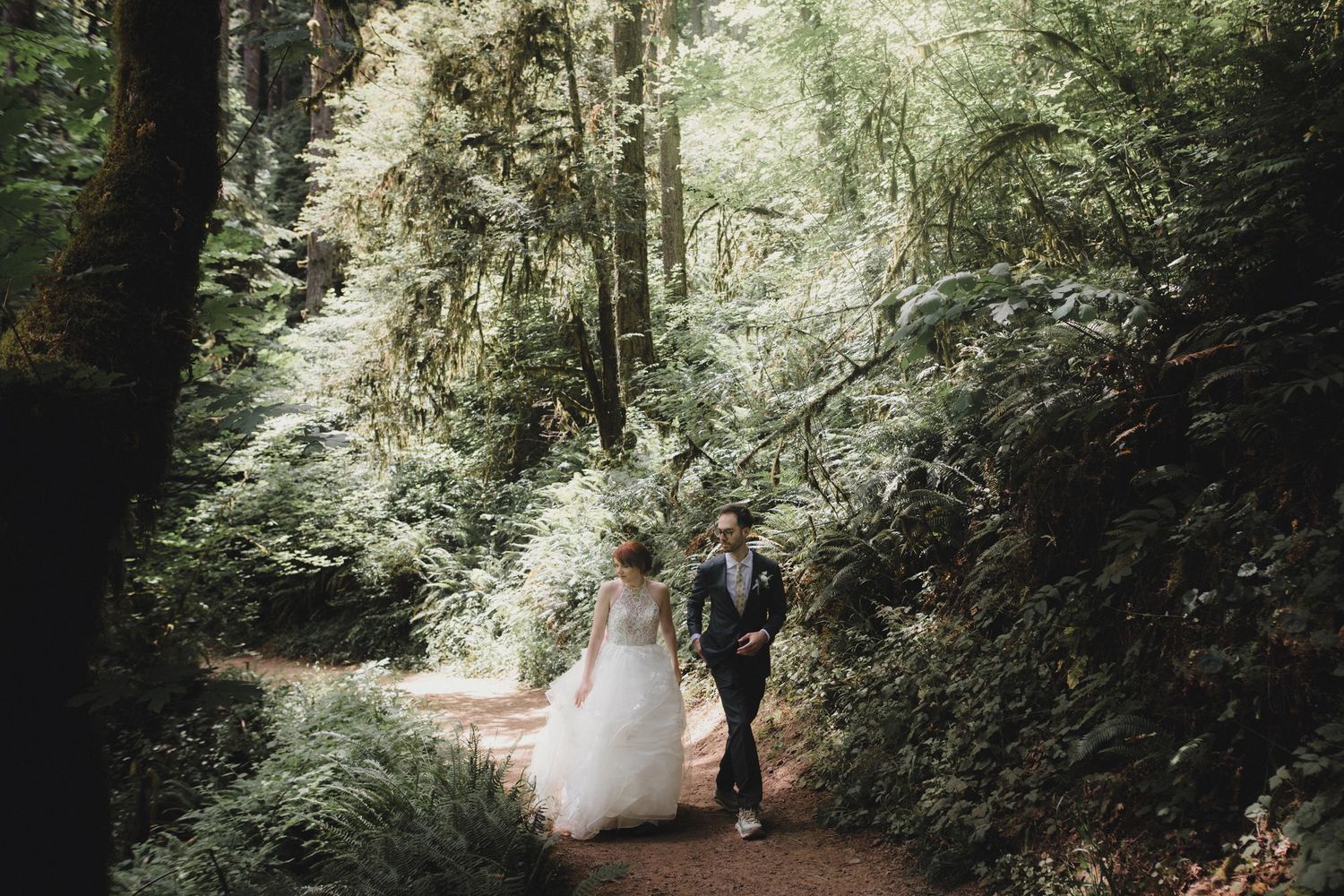 A couple shares a private moment together in a lush forest setting during what appears to be a wedding ceremony.