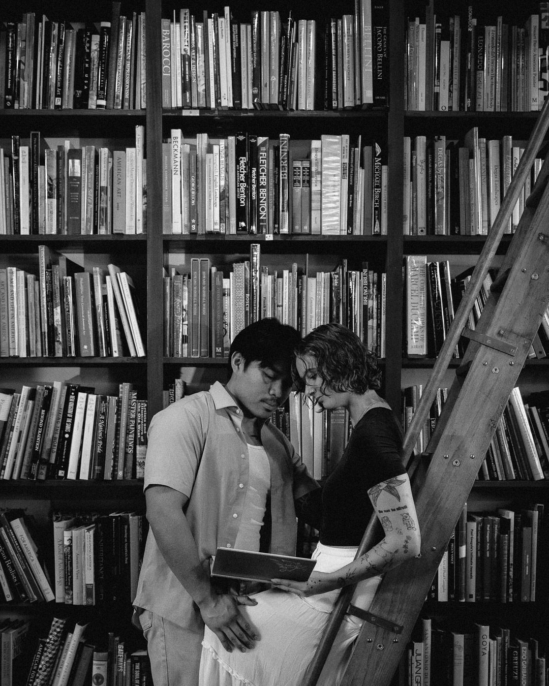 A girl sits on a wooden ladder while her boyfriend reads over her shoulder.