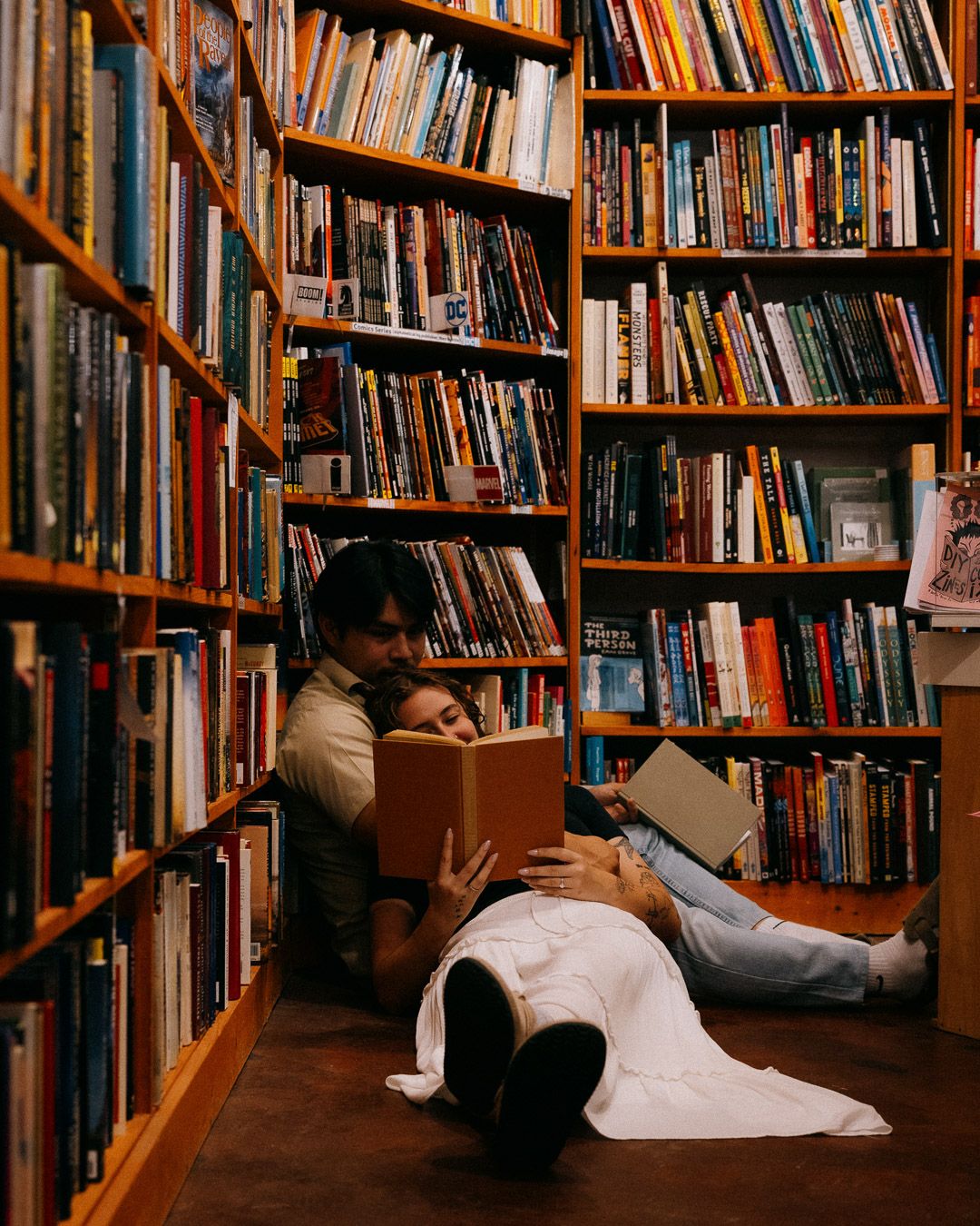 A couple sitting on the floor of a bookstore next to each other, reading.