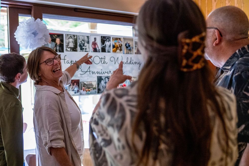 A group of people looking at and discussing photos displayed on a wall in an indoor setting.